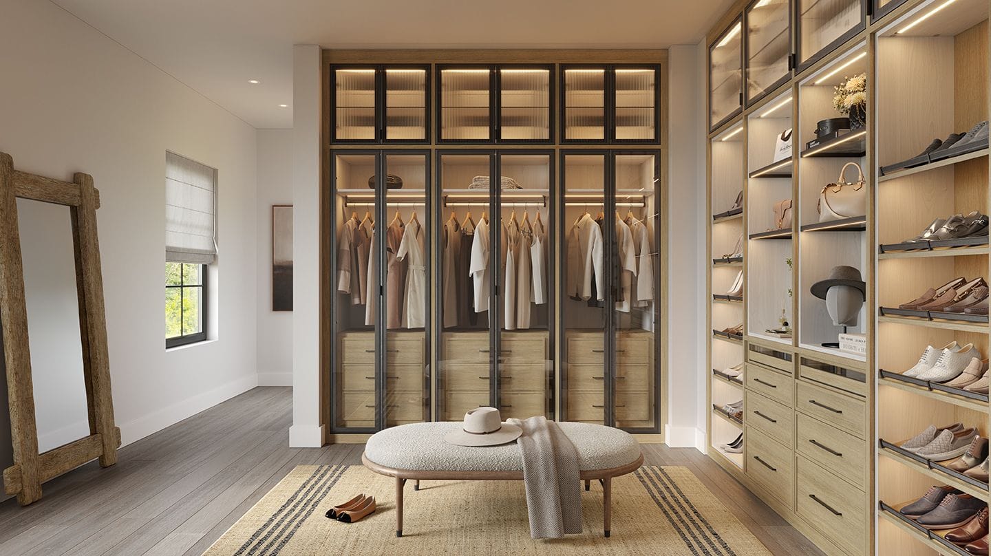 A walk in closet layout designed with custom lighting, shoe storage and seating area by California Closets