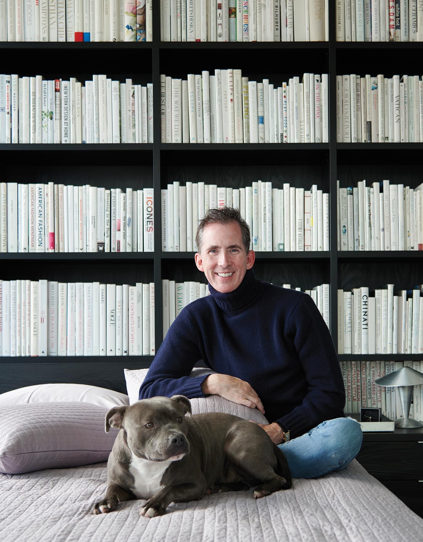 Sharkey and Tio relax together in Sharkey’s bedroom, filled with books on every wall — one with all white (shown here), one with all black, and one organized by color in Ideas of Order Magazine